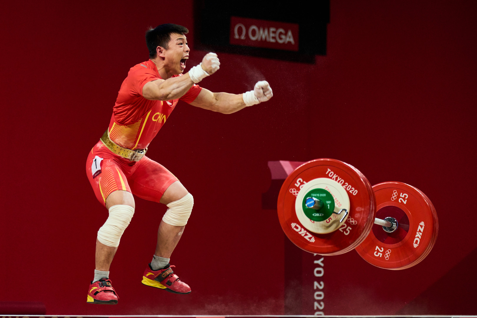 Chinese weightlifter celebrating lift whilst jumping with clenched fists.