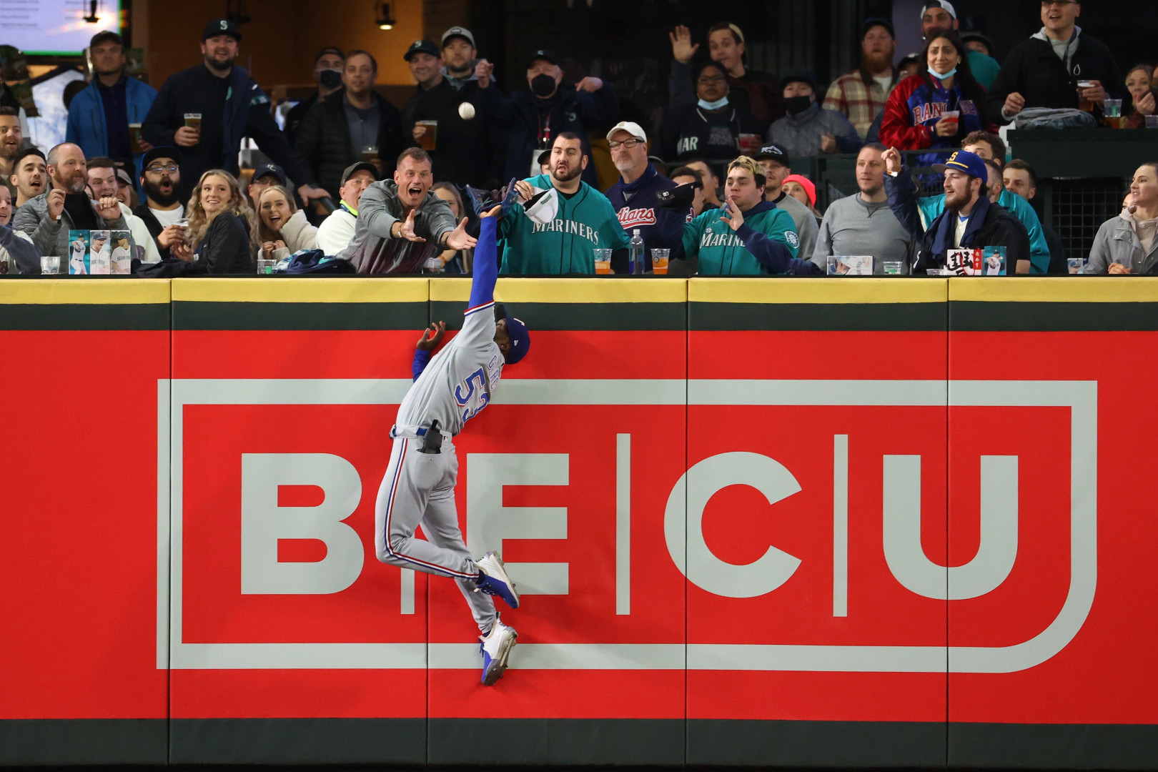Baseball fielder jumping high to stop baseball flying into the crowd.