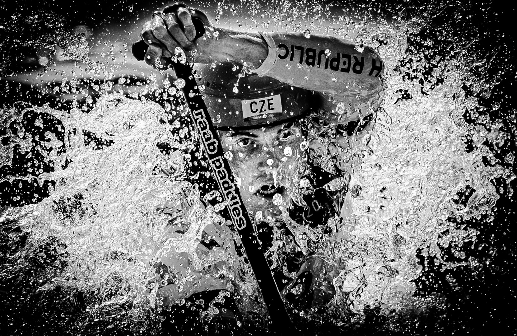 Black & White image of kayaker bursting through water with paddle.