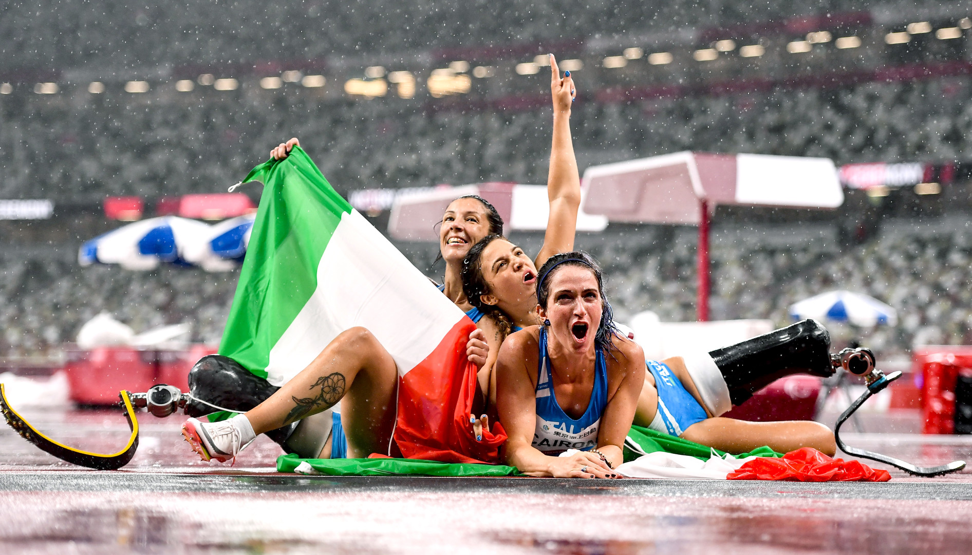 Female Italian Paralympic althetes piled on the track at the finish line.