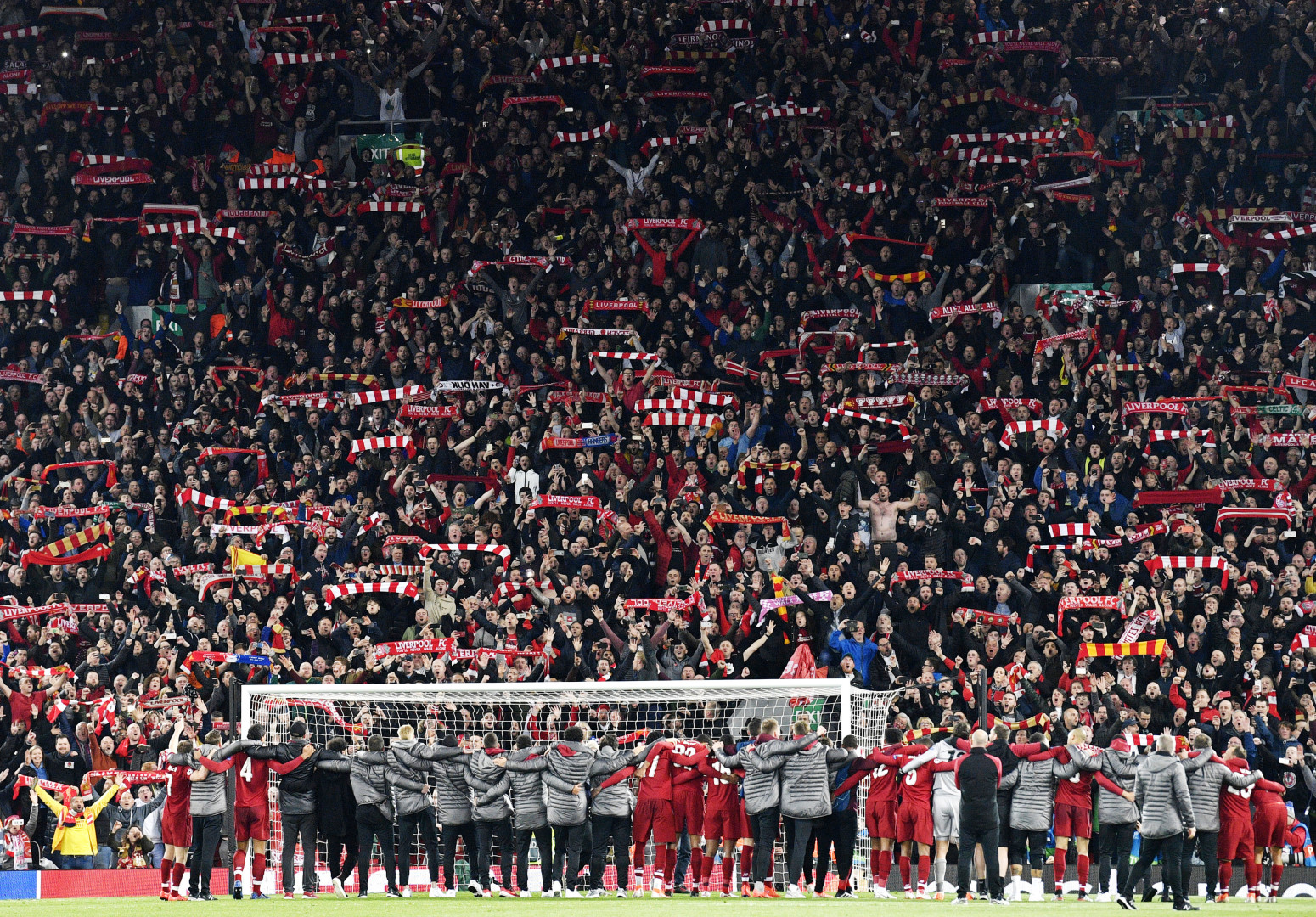 Liverpool players celebrate in front of crowd of fans holding Liverpool scarves in the air.