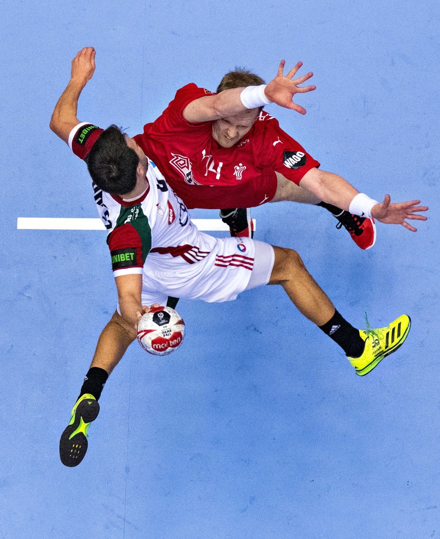 Two opposing handball players colliding to stop a shot for goal.