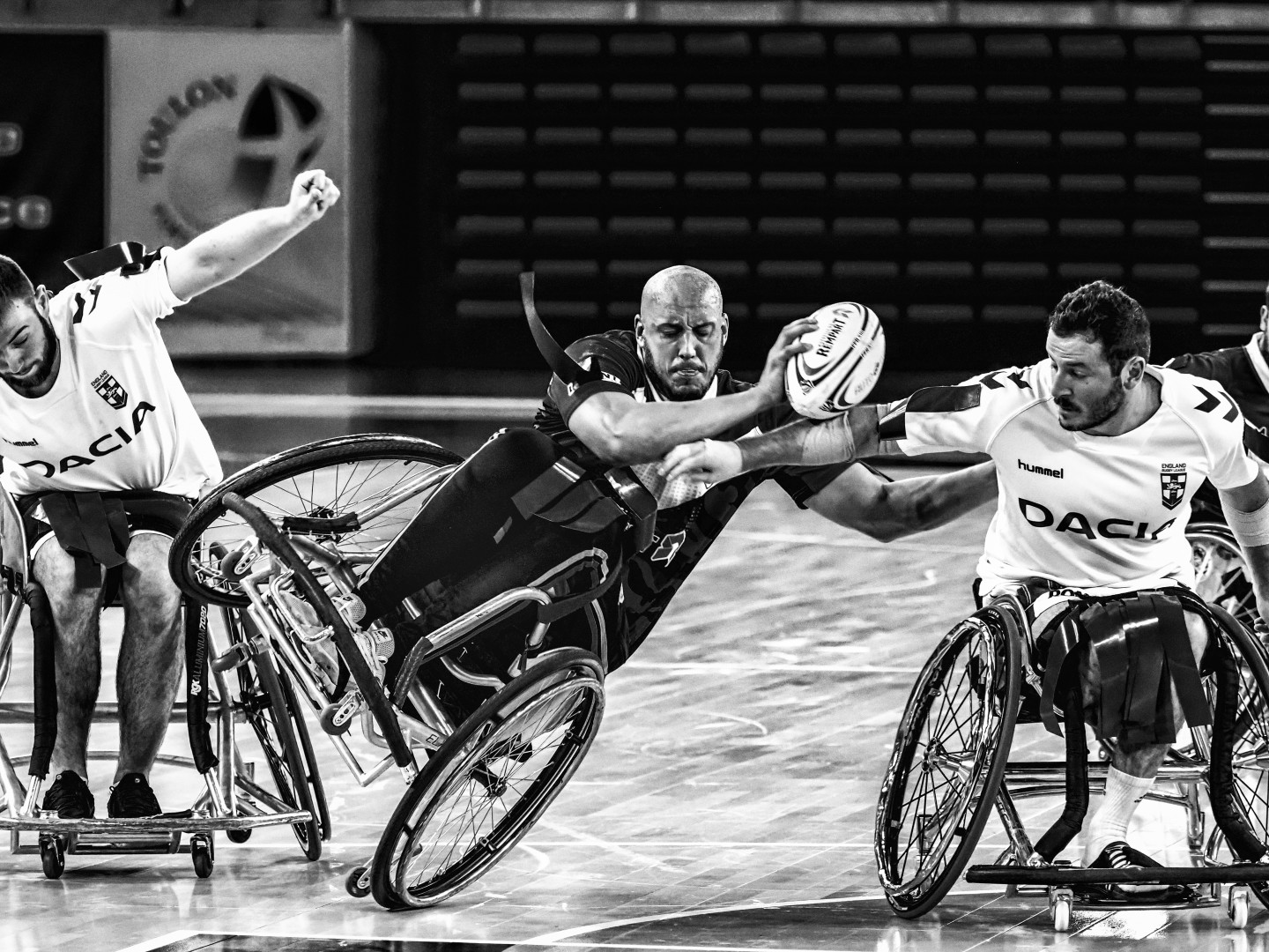 Wheelchair rugby player mid fall as tackled by two opponents.