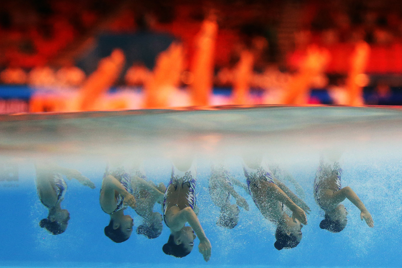 Half and half underwater photograph of synchronised swimmers upside down during routine.