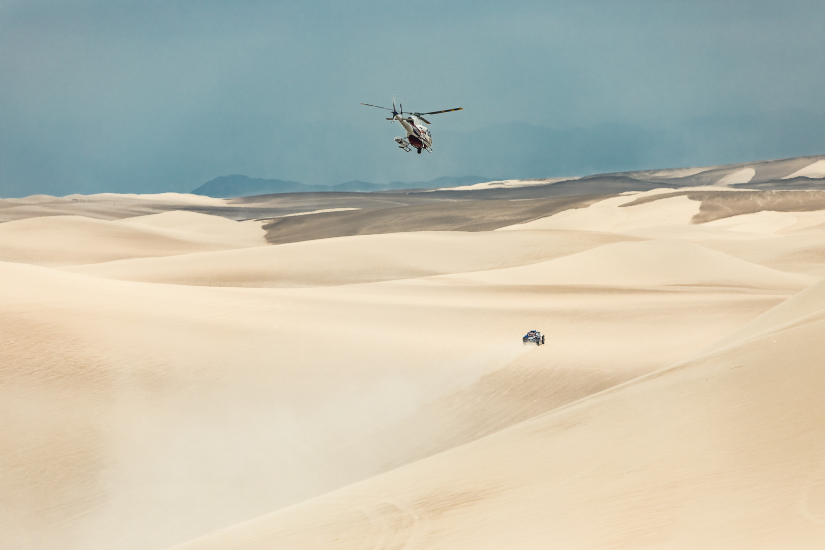 Helicopter following a dune buggy across the fast open desert.