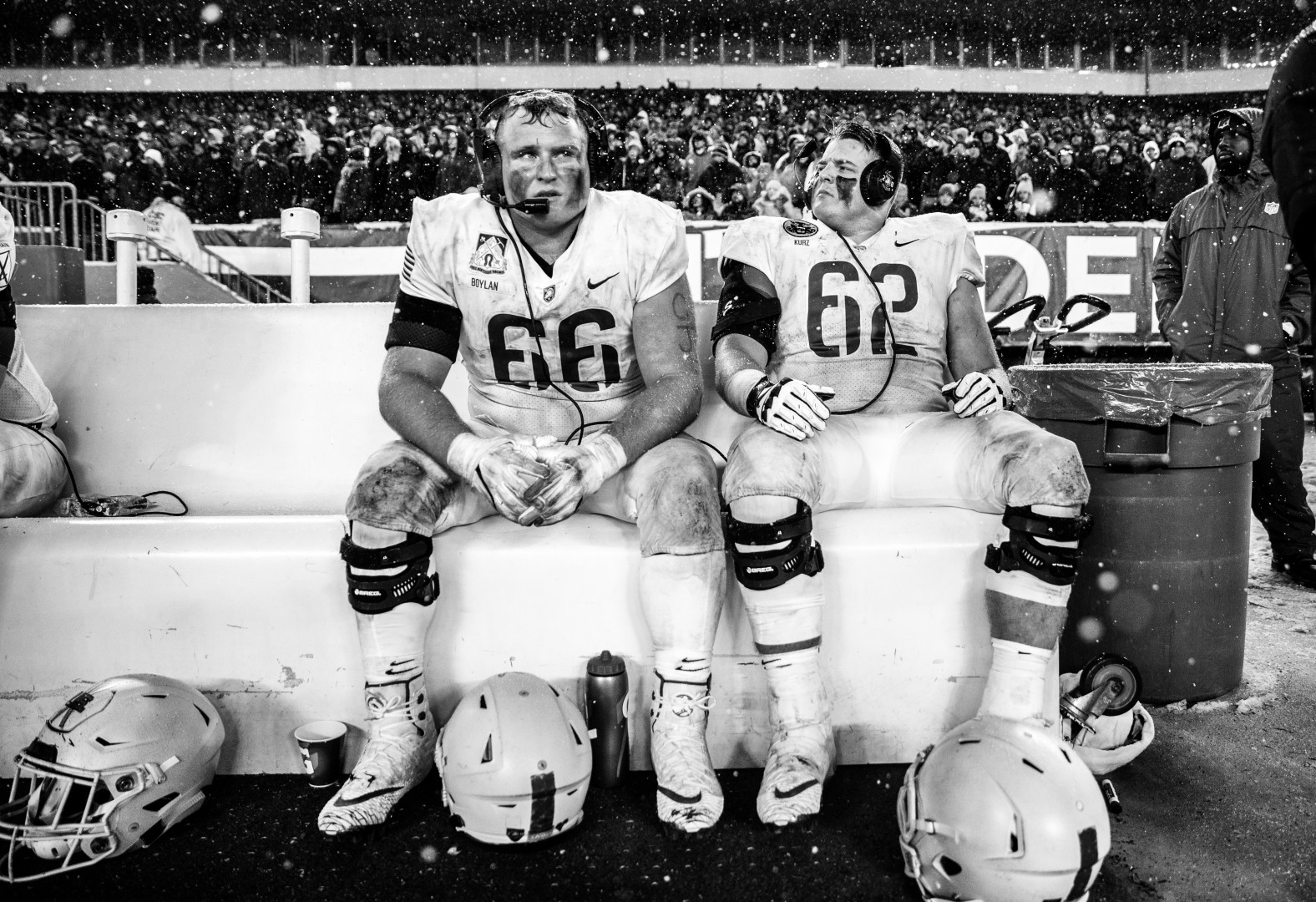 Black & White photograph of two subbed off players listening to the commentary of the game through headphones at the side of the pitch.