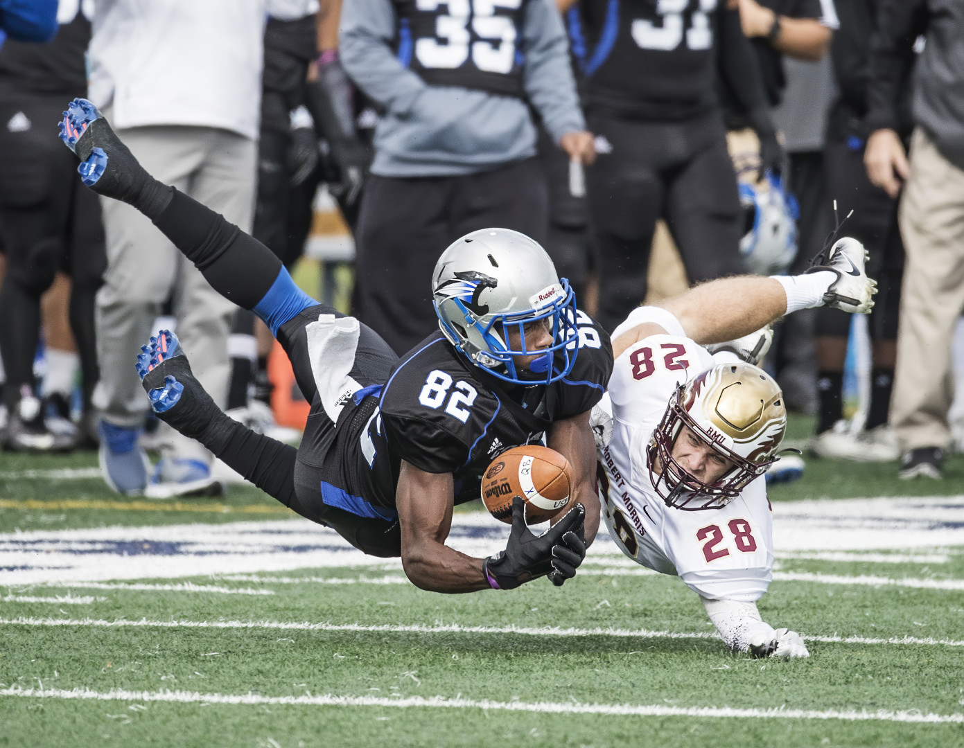American Football player mid catch on touch down whilst opposing player attempts to tackle.