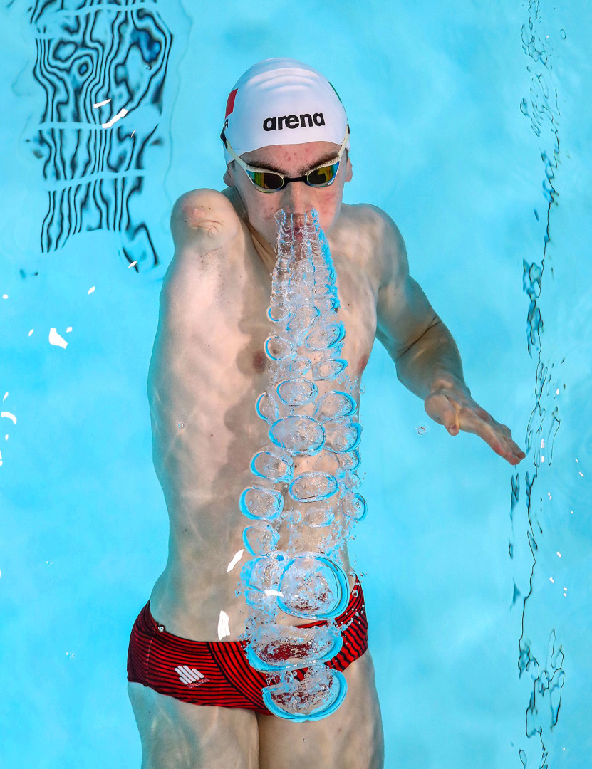 Paralympic swimmer blowing out trumpet of bubbles in backstroke length of race.
