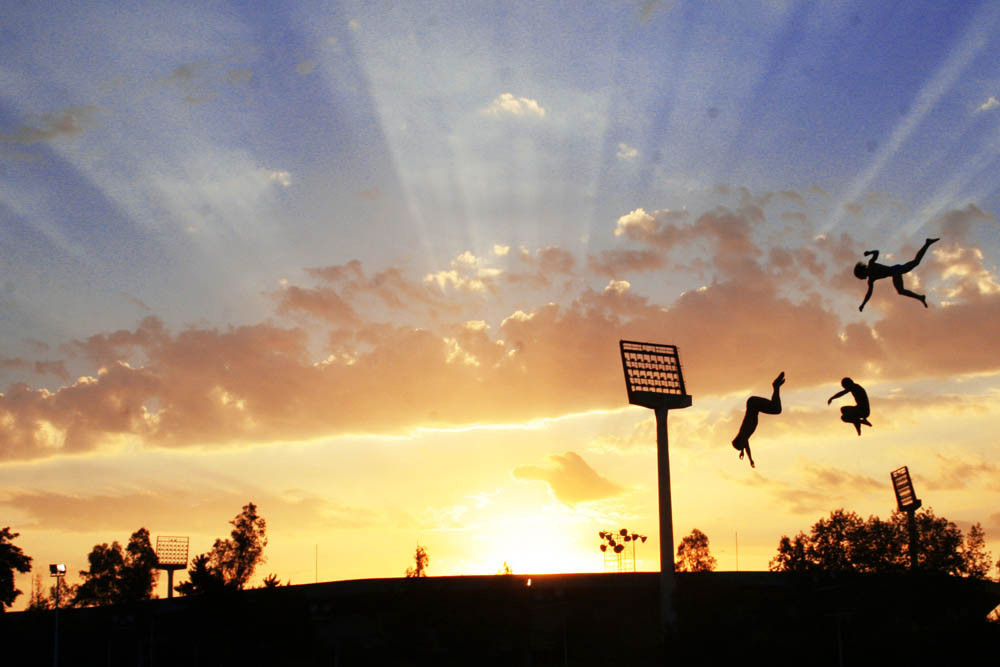 Three divers freestyle jumping of an outside diving platform at sunset.