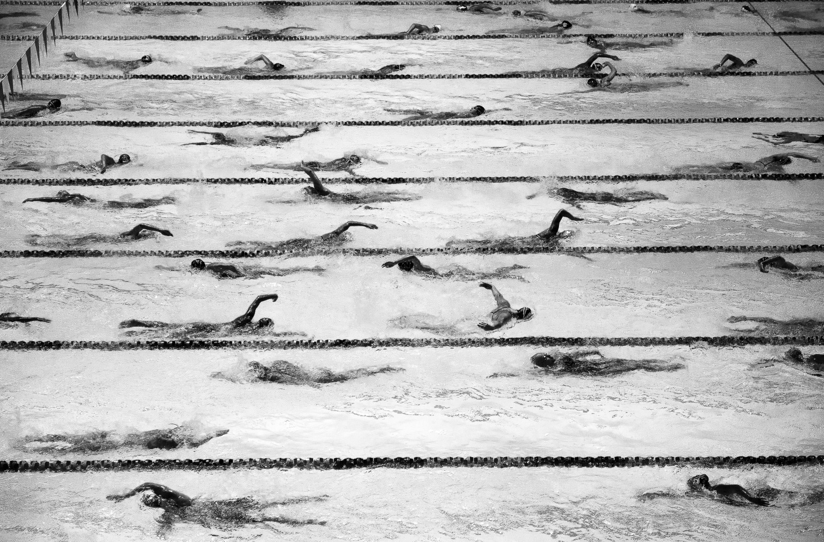 Black & White photograph of swimmers doing circuits of lanes in a swimming pool.