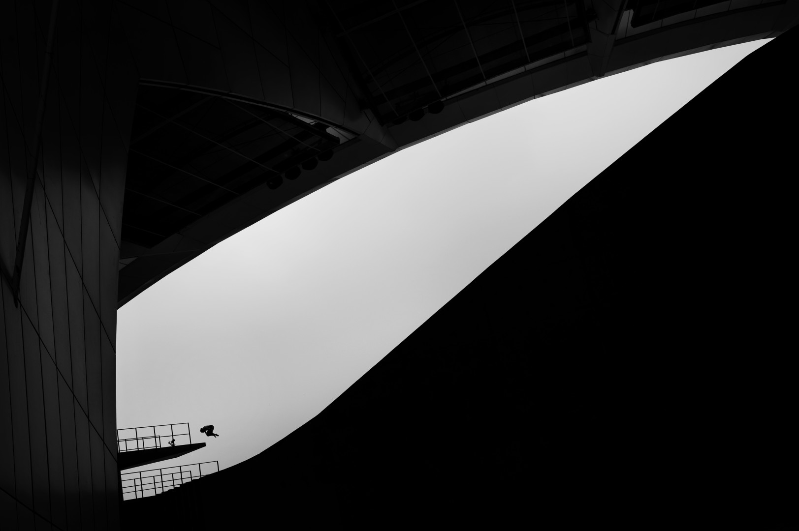 Black & White photograph of diver jumping off of a platform, highlighted by a sliver of light.