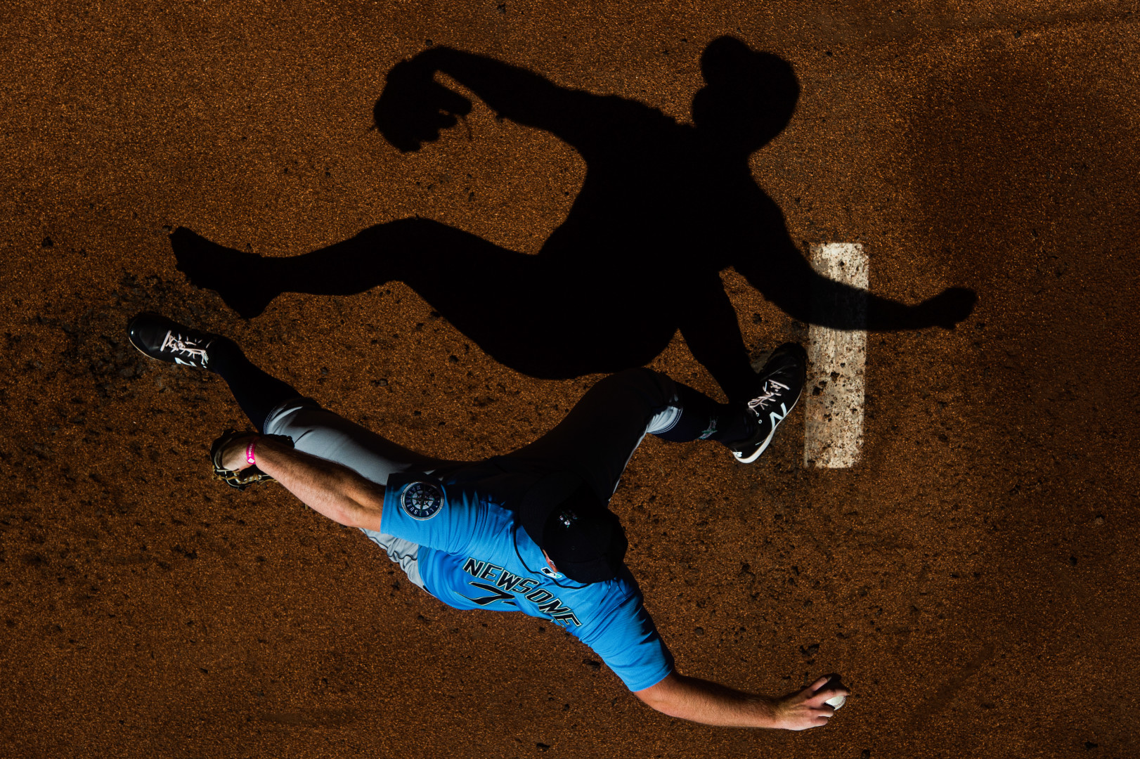 Birdseye view photograph of baseball player's silhouette on the pitch as he throws baseball.