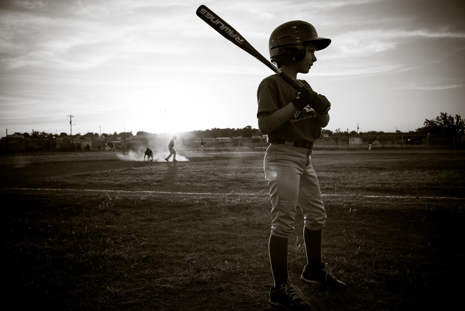 Black & White photograph of young baseball player standing with bat over his shoulder on the field.