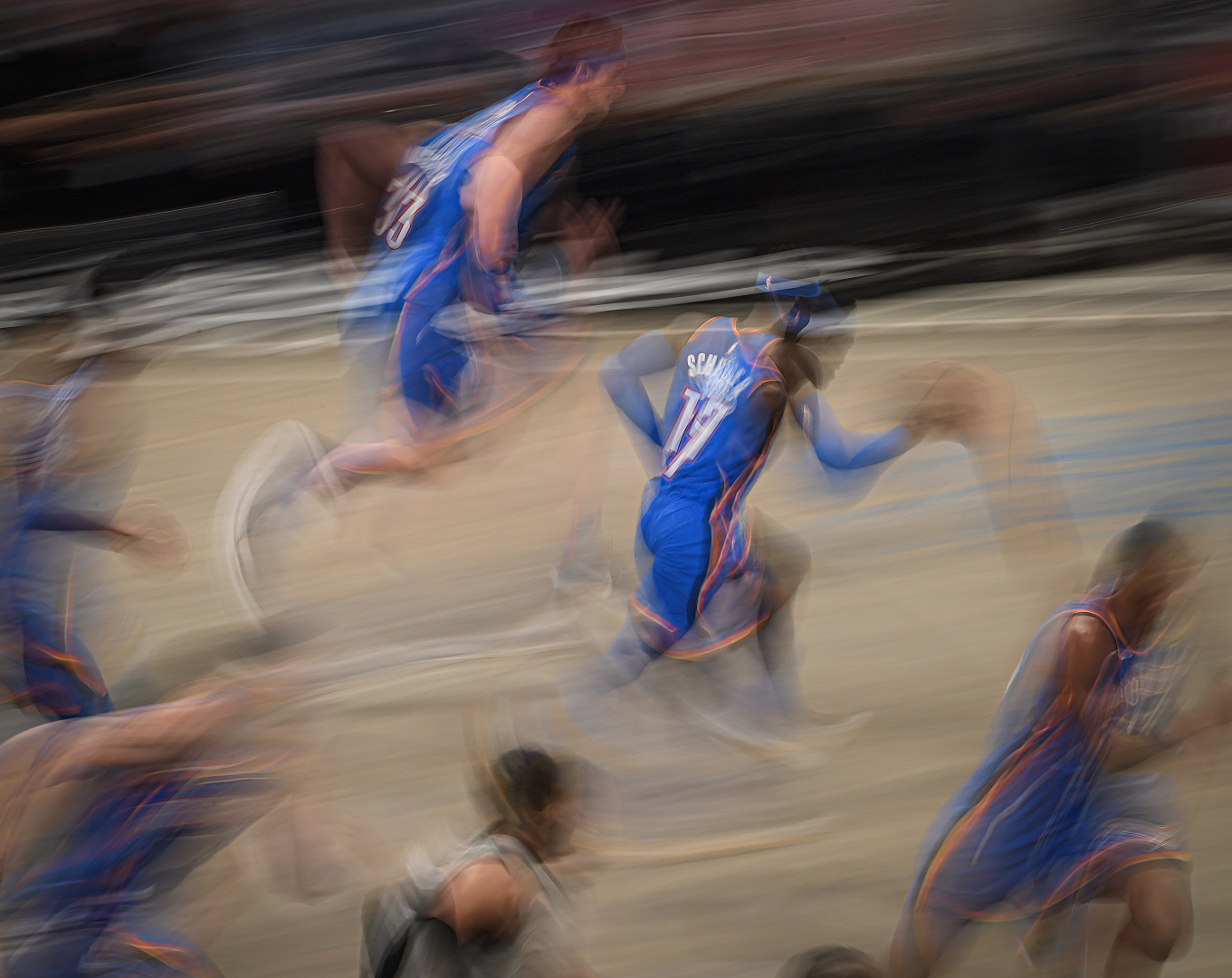 Blurred action shot of basketball team running down the court with ball.