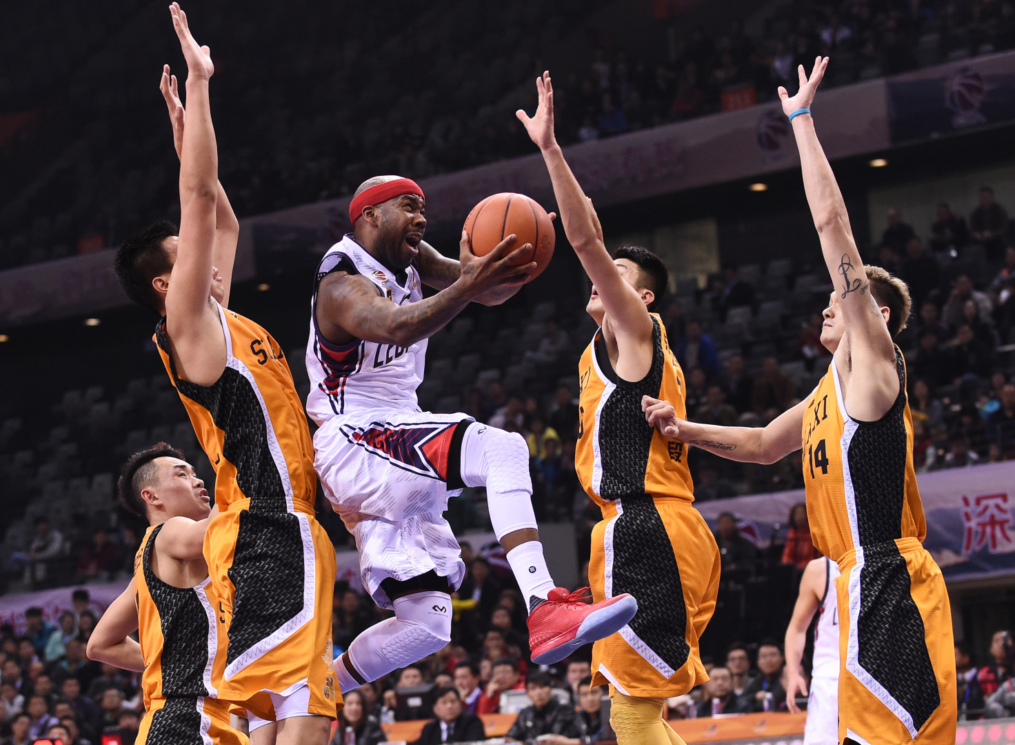 Basketball player mid jump surrounded by four opposing players with their arms high in a defensive position.