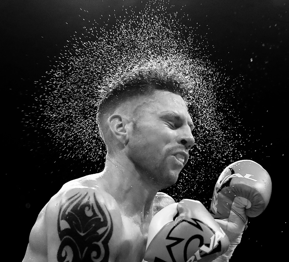 Black & White photograph of sweat spraying from boxer after hit.