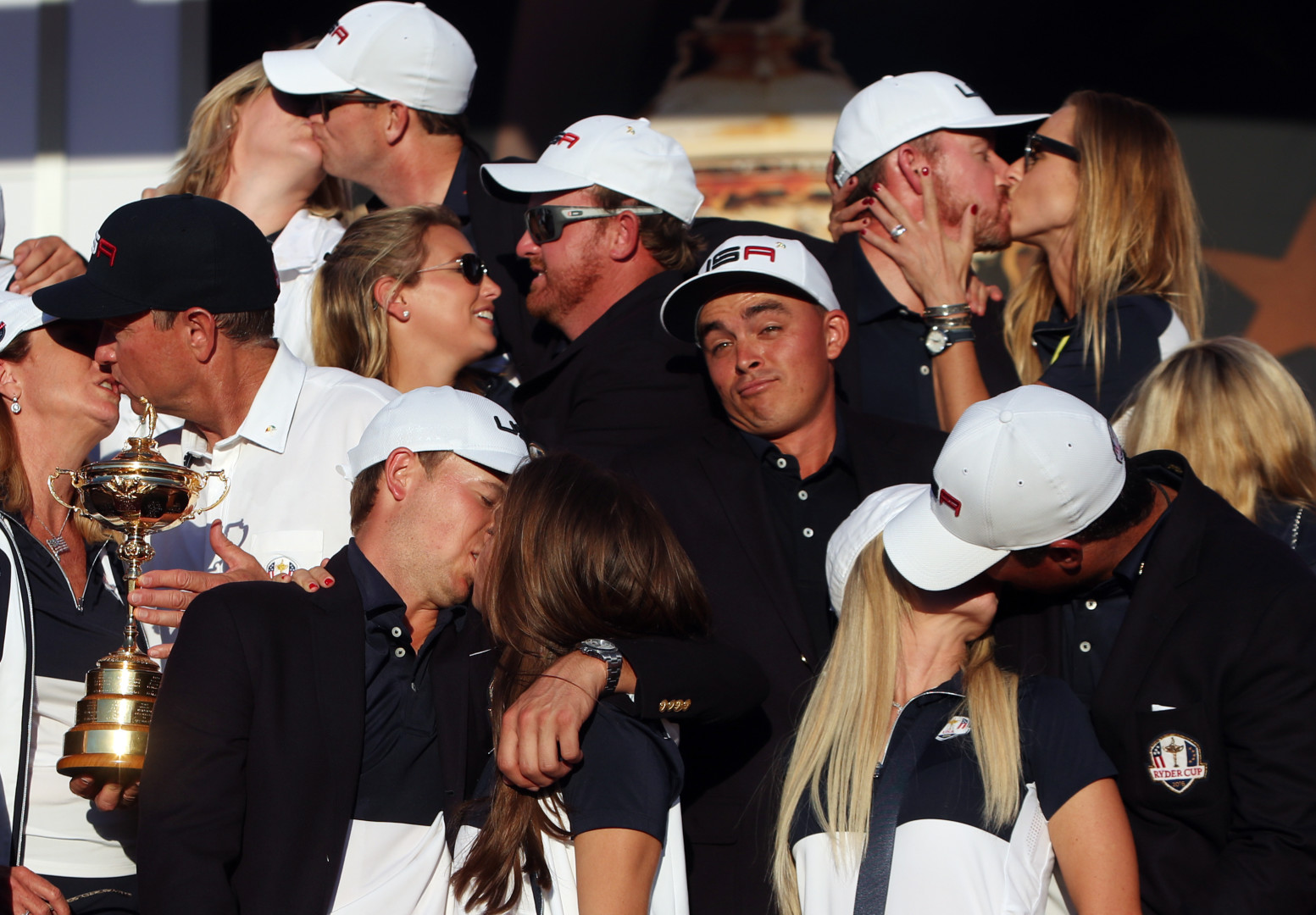 Single golfer surrounded by fellow winning golfers kissing their partners.