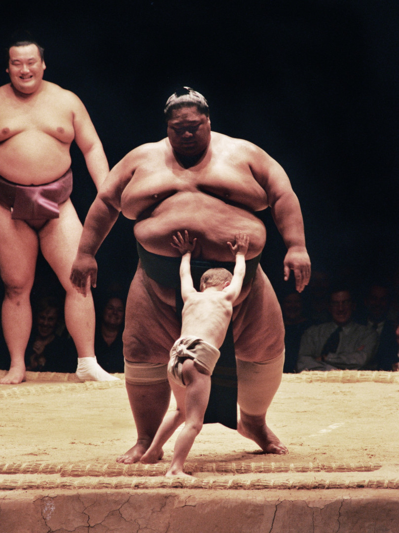 Young boy trying to push big Sumo Wrestler out of the ring.