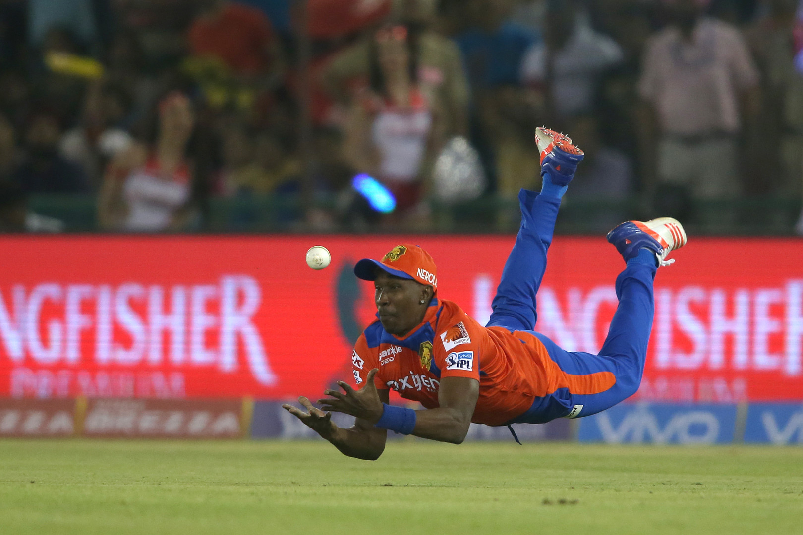 Cricket playing in red and blue kit, diving to catch a ball.
