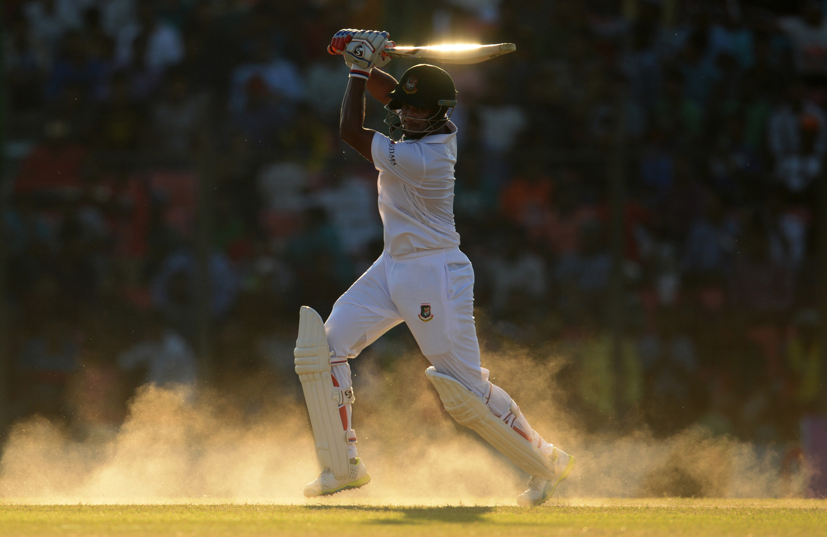 Shakib Al Hasan swinging for a hit in the hazy, sandy dust of the cricket pitch.