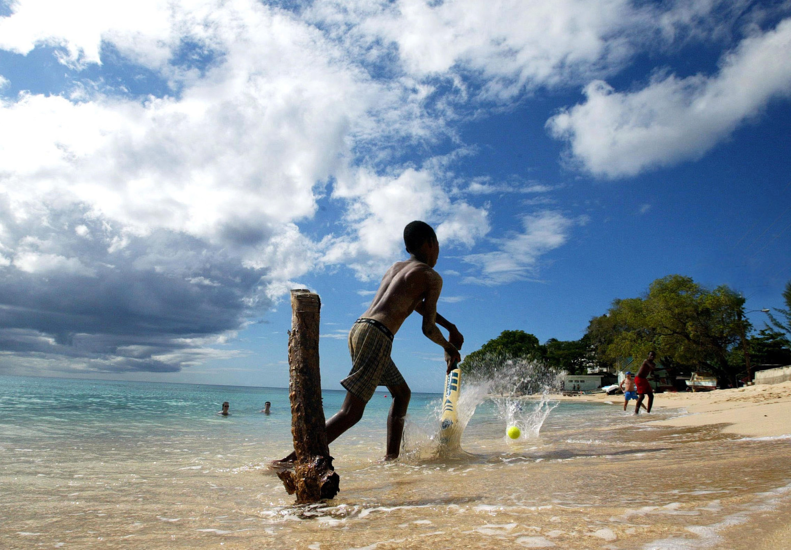 Young boys playing beach cricket in the shallows of the sea.