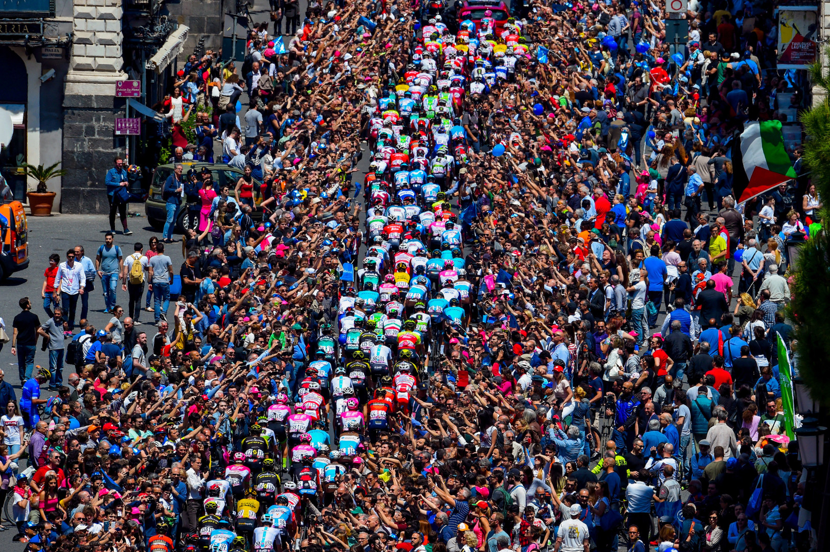 Trail of cyclists moving up the hill as swarms of people line the streets to take photos.