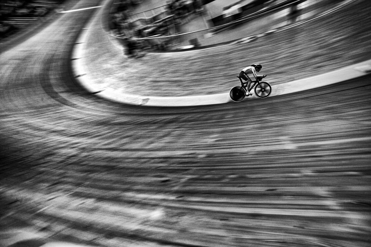 Black & White slanted, blurred action shot of cyclist speeding around Velodrome track.