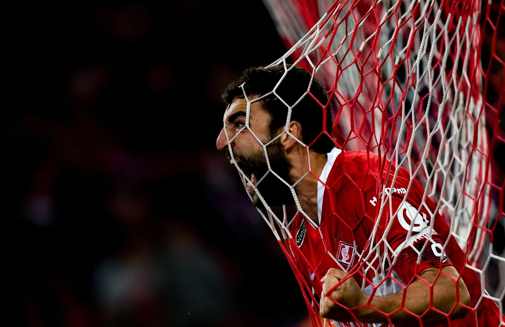 Football player shouts at crowd as his face pushes through football net.