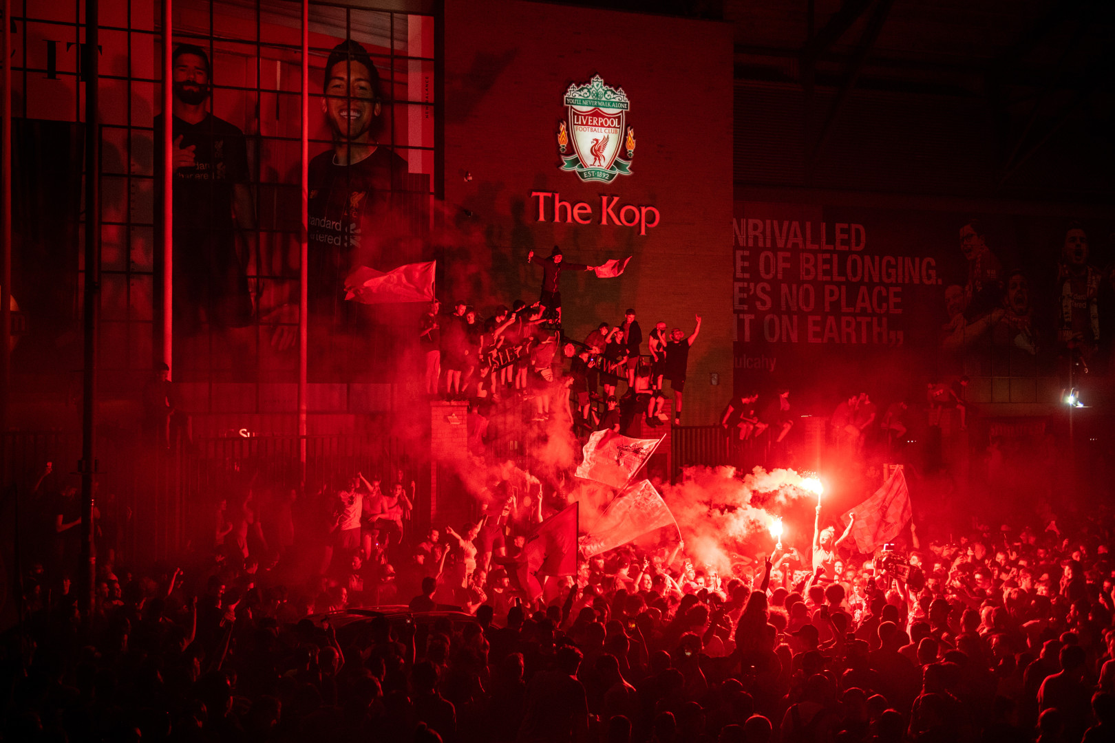 Liverpool fans celebrating league win outside The Kop with flares and flags.