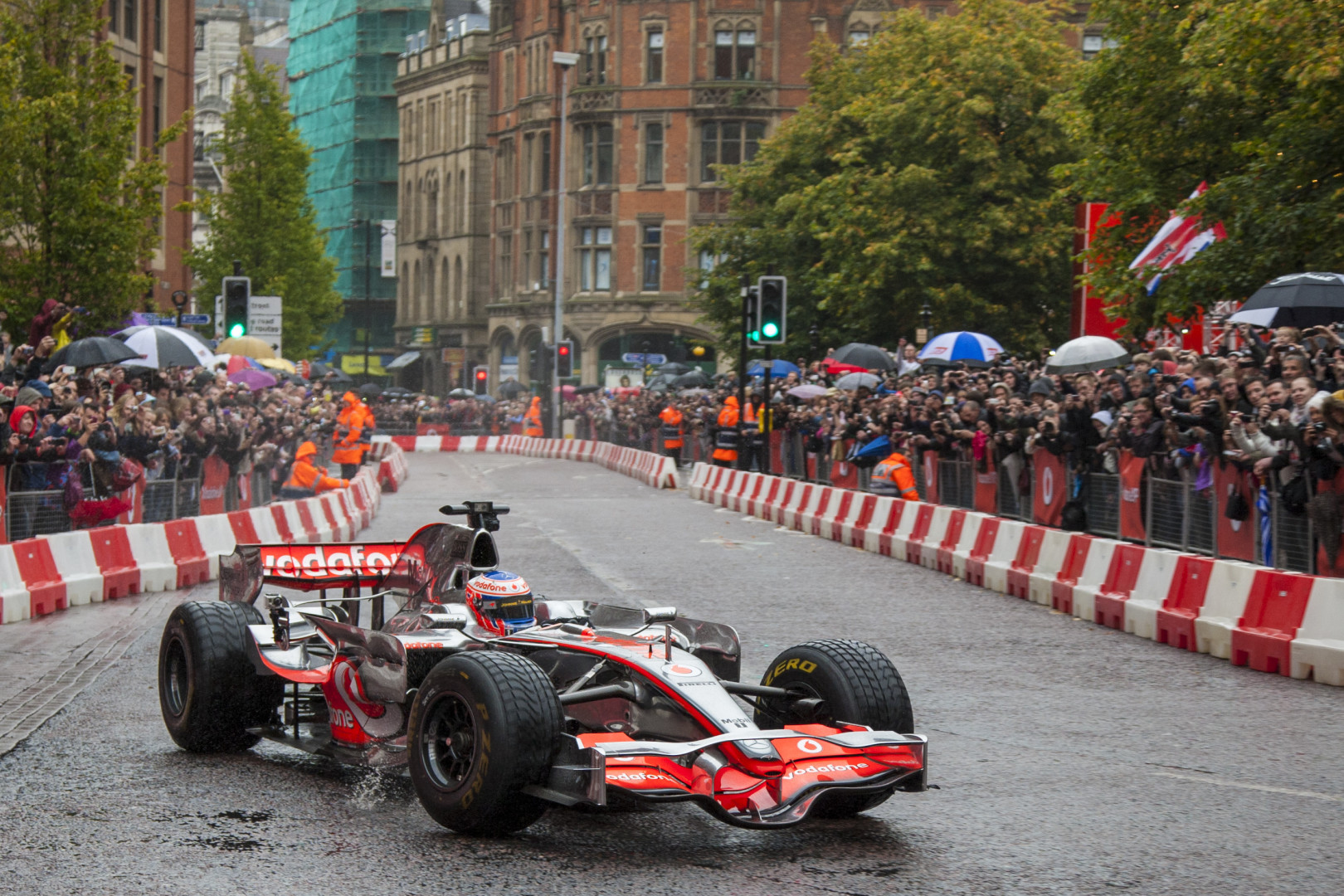 Formula 1 car racing through city streets lined with crowds of people.