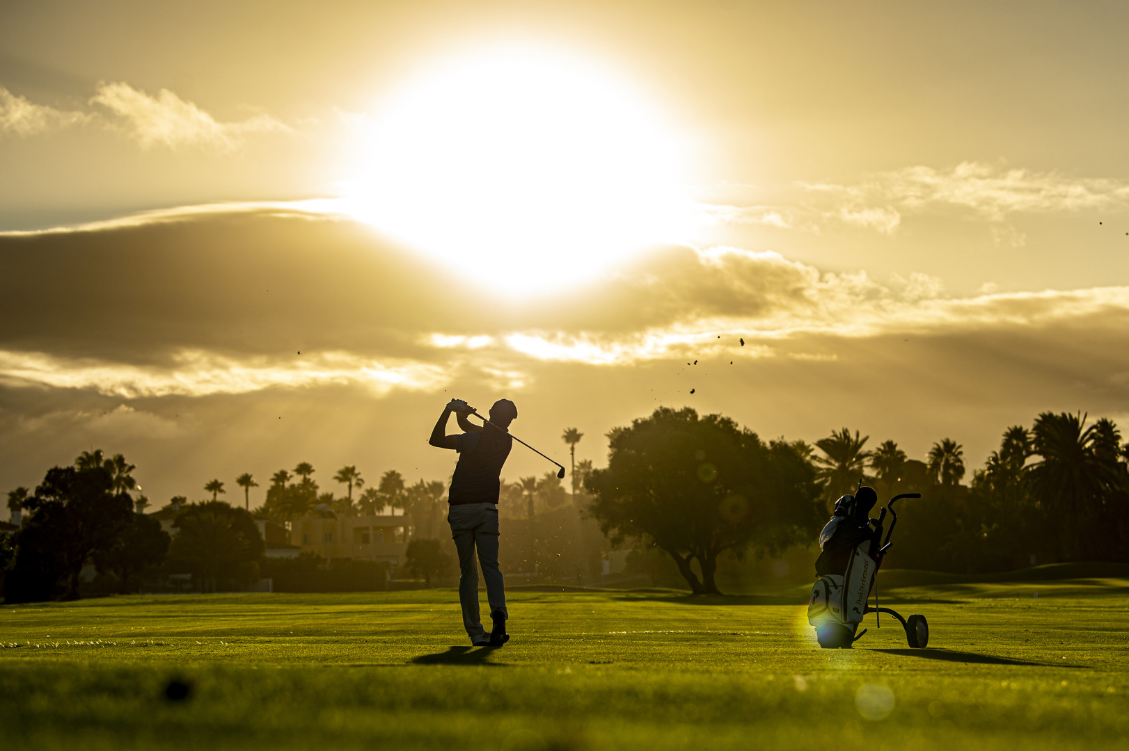 Bjorn Hellgren hitting the golf ball on the golf course as the sun bursts from behind the clouds.