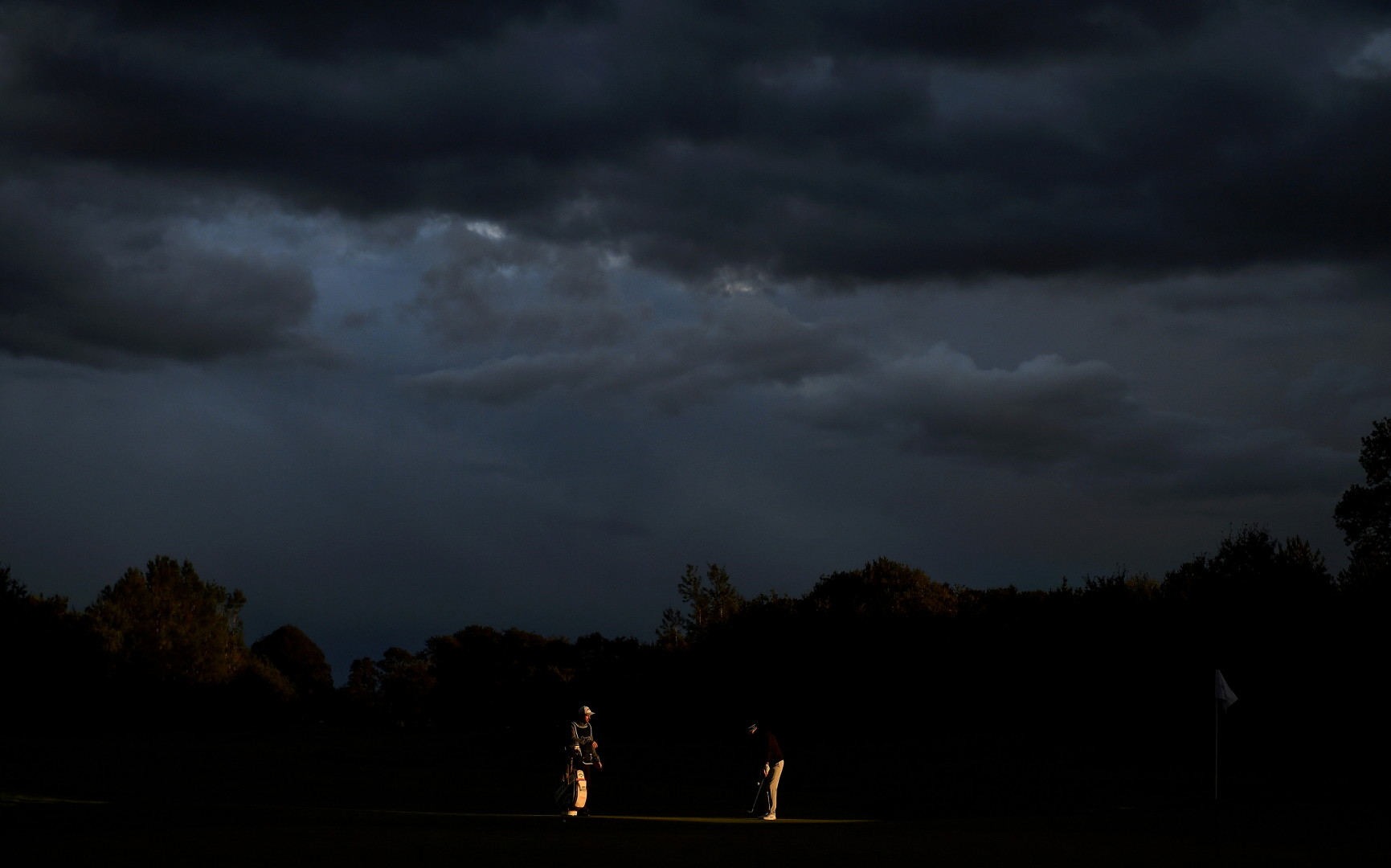Two golfers highlighted by a strip of light as they put for an evening game of golf.