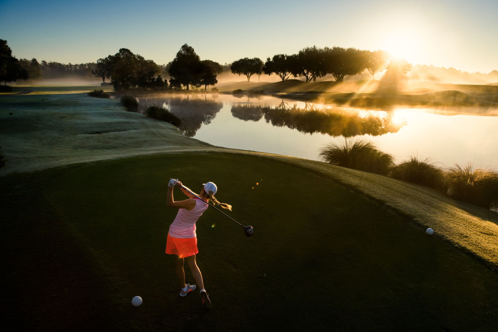 Female golfer hitting the ball across the course at sunrise.