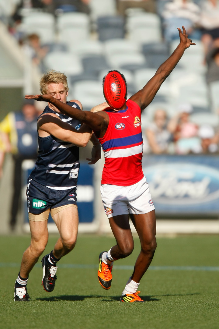 Aussie Rules Football player's head blocked from view as ball bounces up and covers face.