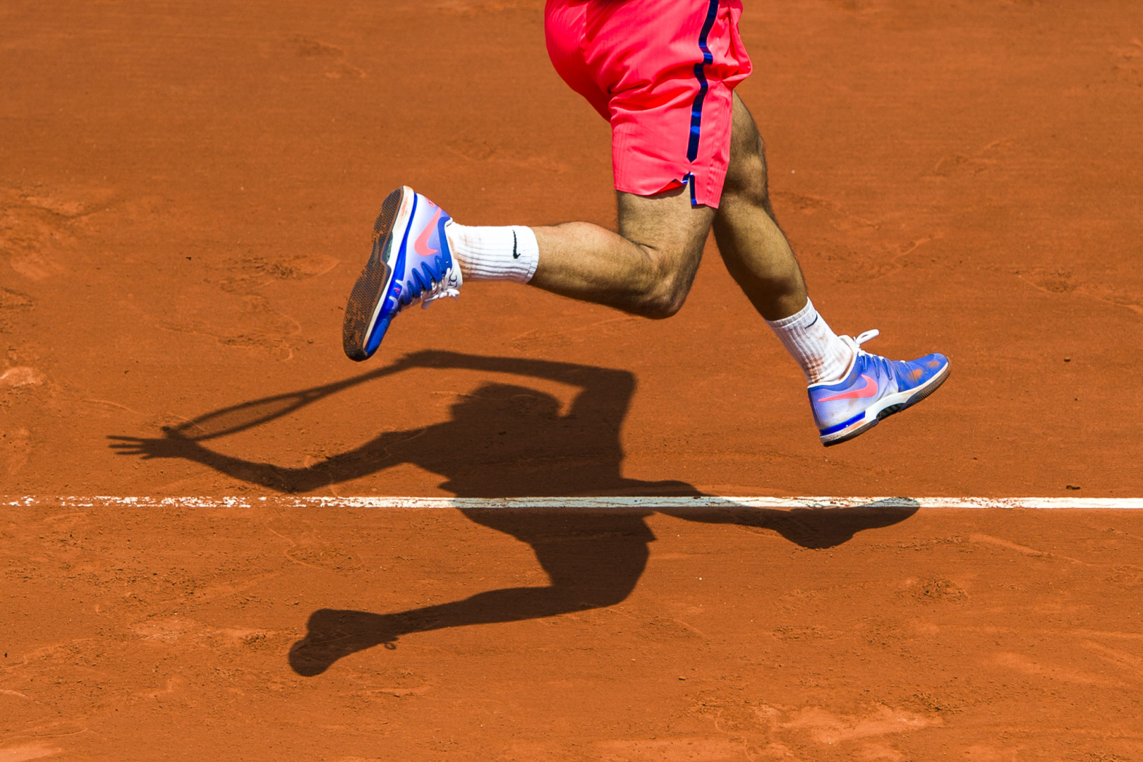 Tennis player's legs and shadow on court as they jump.