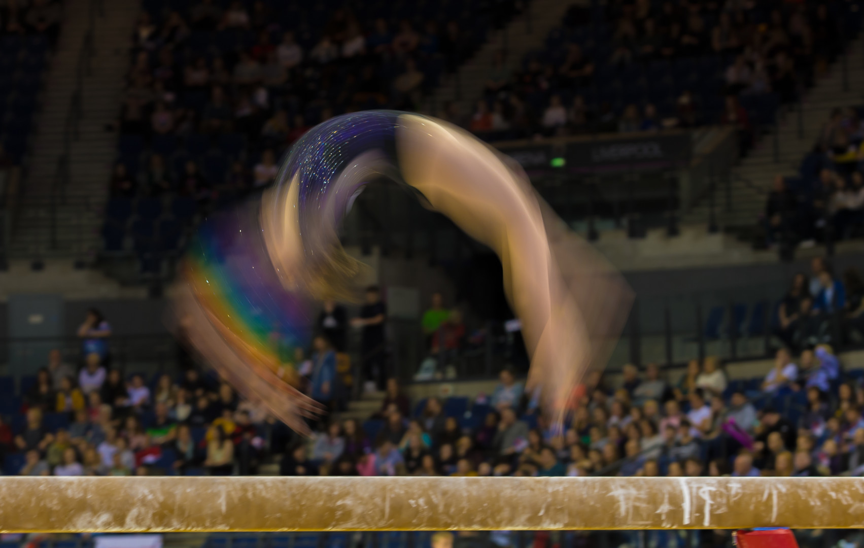 Artistic beam gymnast in motion as she carries out flip in routine.