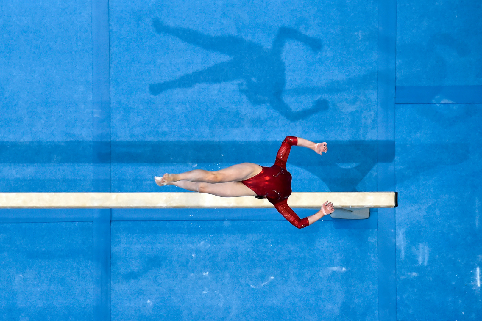 Birdseye shot of female gymnast mid flip on balance beam routine.