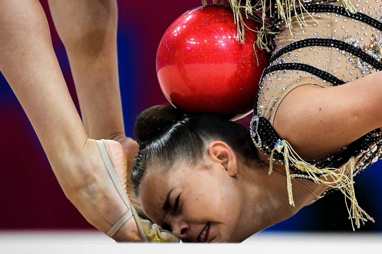 Head shot of female rhythmic gymnast performing a backwards role with a ball during routine.