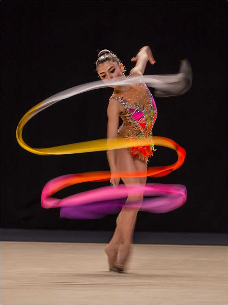 Female rhythmic gymnast twirling a ribbon during routine.