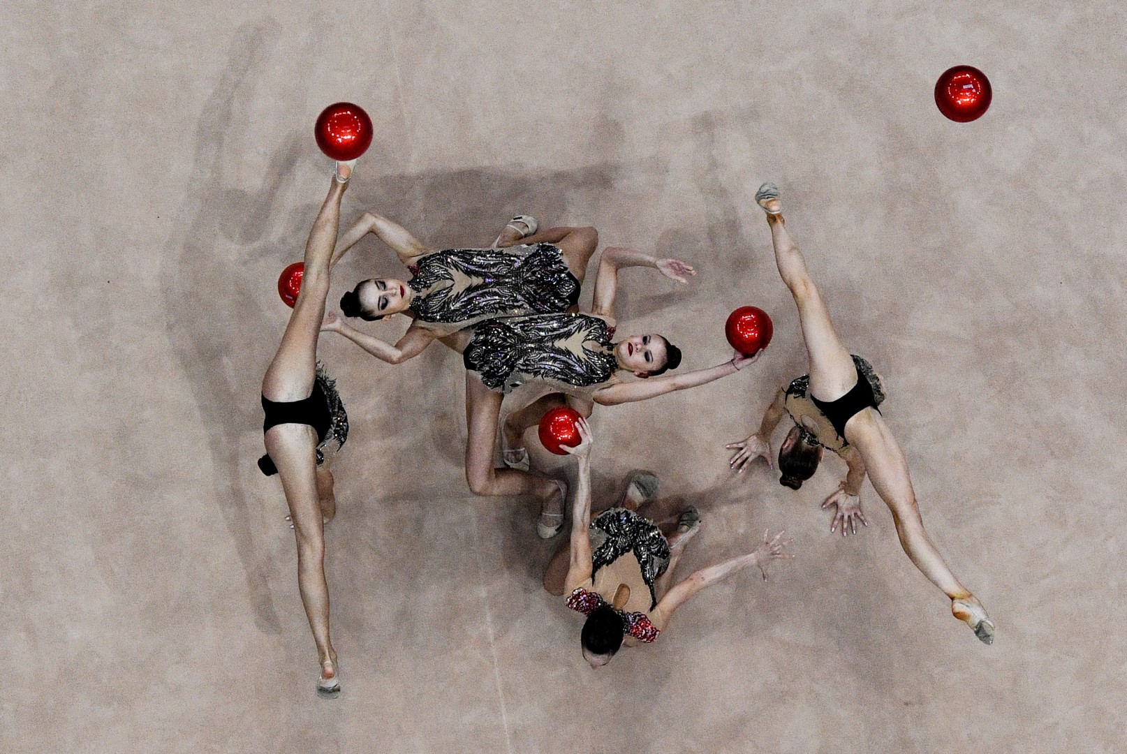 Female rhythmic gymnastic group performing routine with red balls.