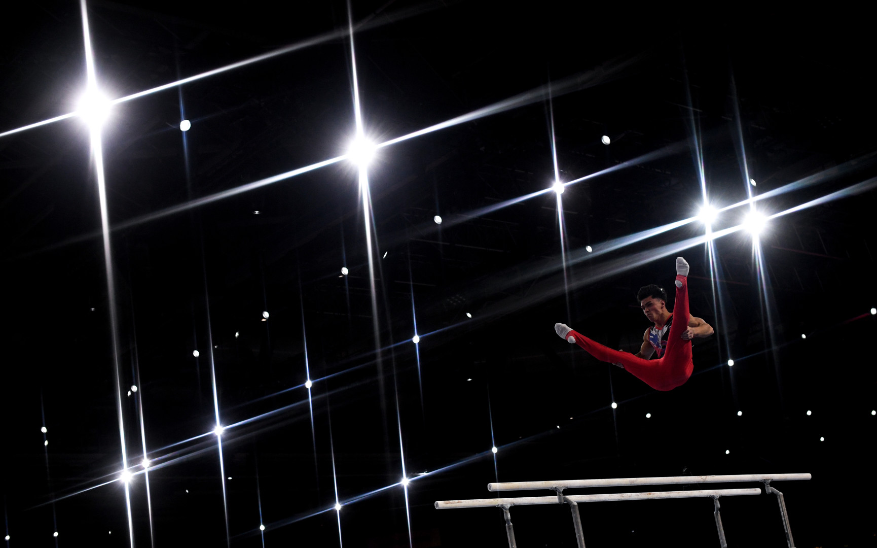 Male gymnast mid air after launching himself from the parallel bars during routine.