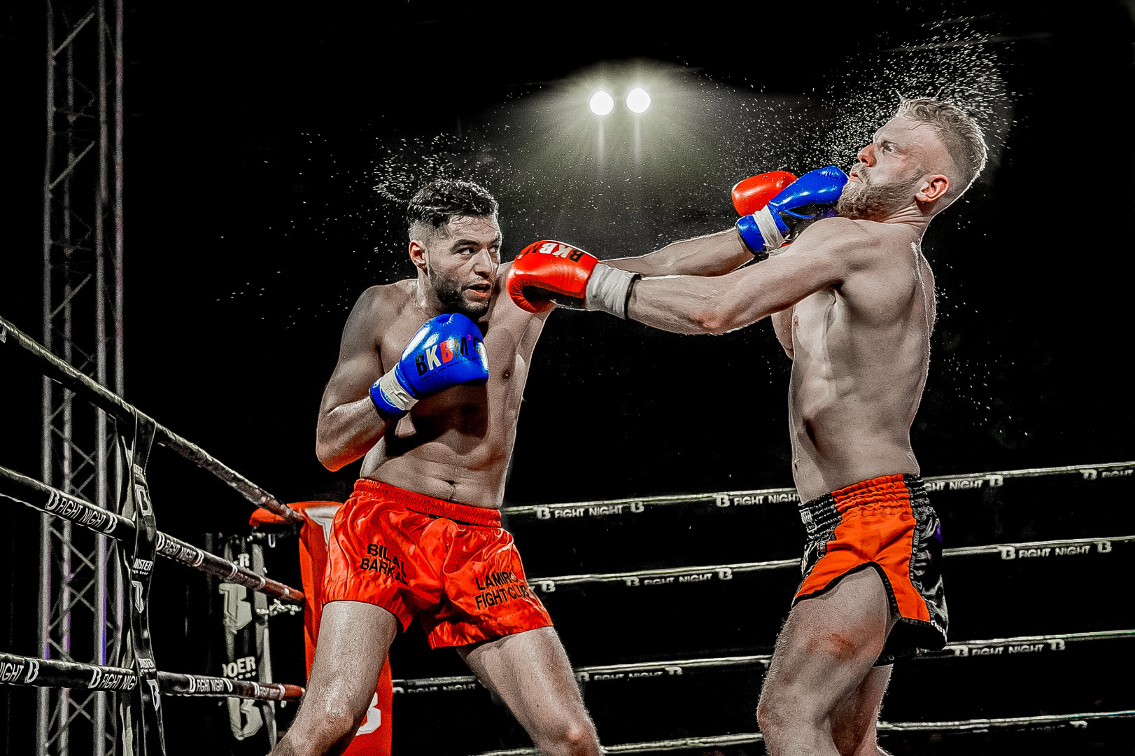 Thai boxing competitor landing huge hit to opponents face as sweat sprays everywhere.