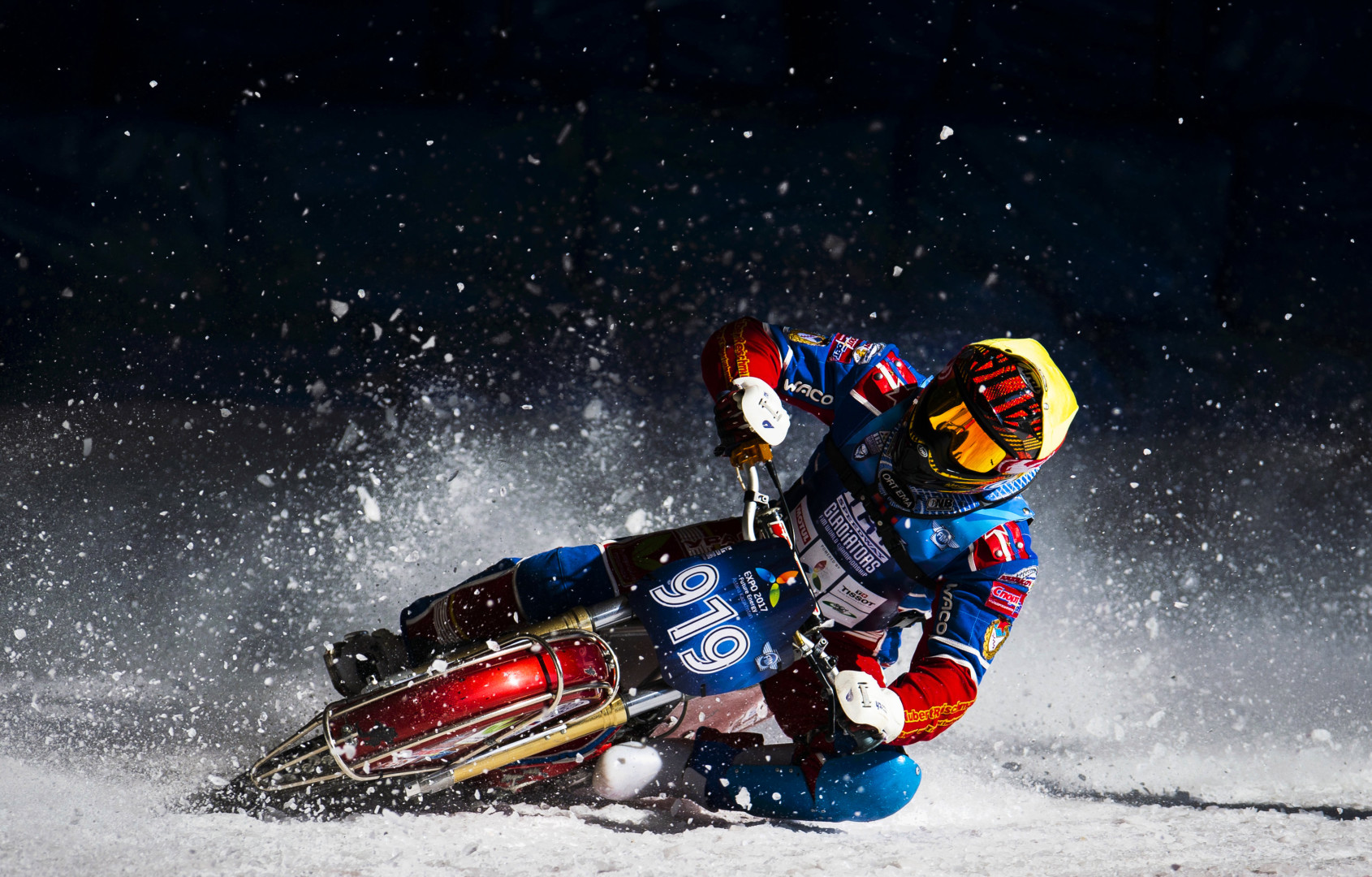Ice Speedway motorcyclist skidding around race track as ice sprays from the back wheel.
