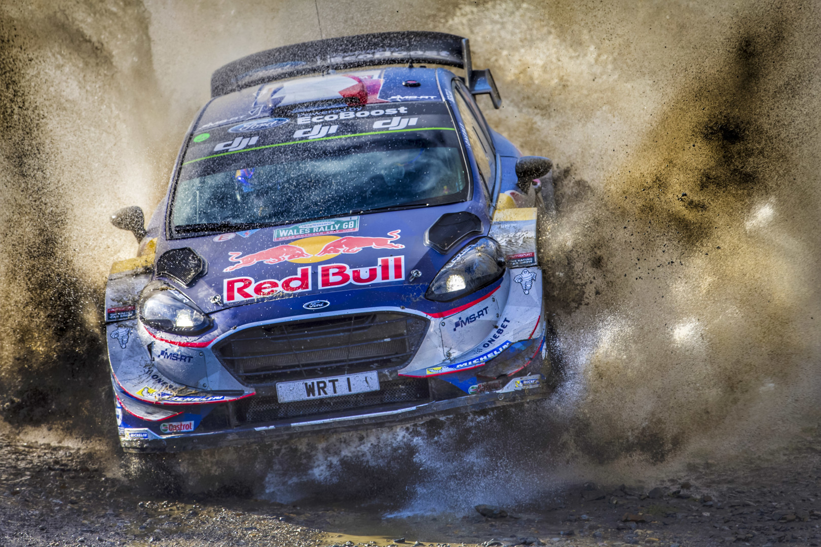 Red Bull motorsport rally car scrambling muddy dirt track.
