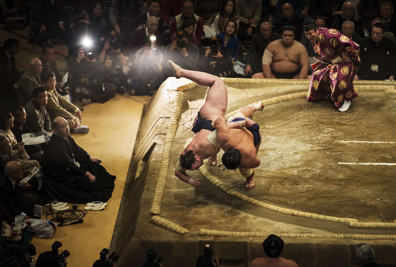 Sumo Wrestling competitor throwing opponent out of the ring as crowd watches.