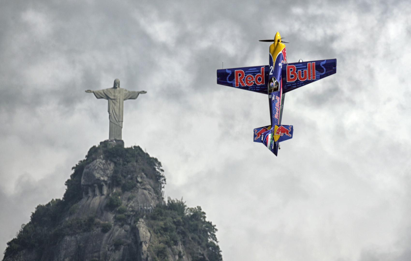 Red Bull stunt plain flying upwards vertically, reflecting the position of the 'Christ the Redeemer' statue in the background.