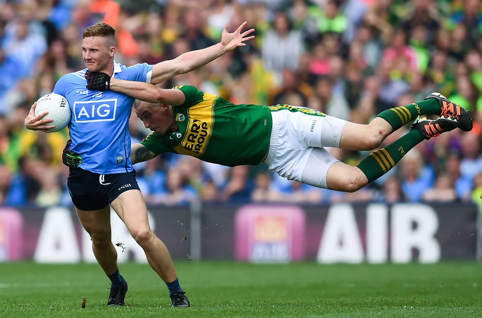 Gaelic footballer flinging himself at opponent in high tackle, whilst opponent stands holding the ball.