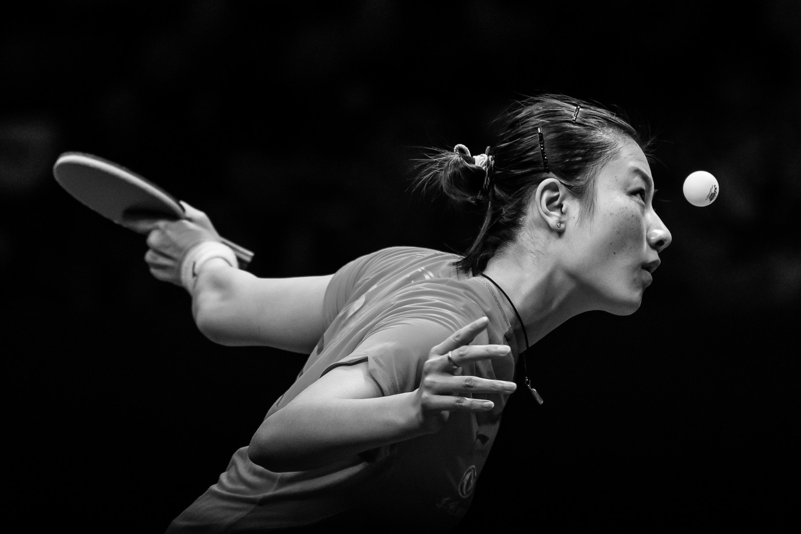 Black & White image of female table tennis player making a serve.