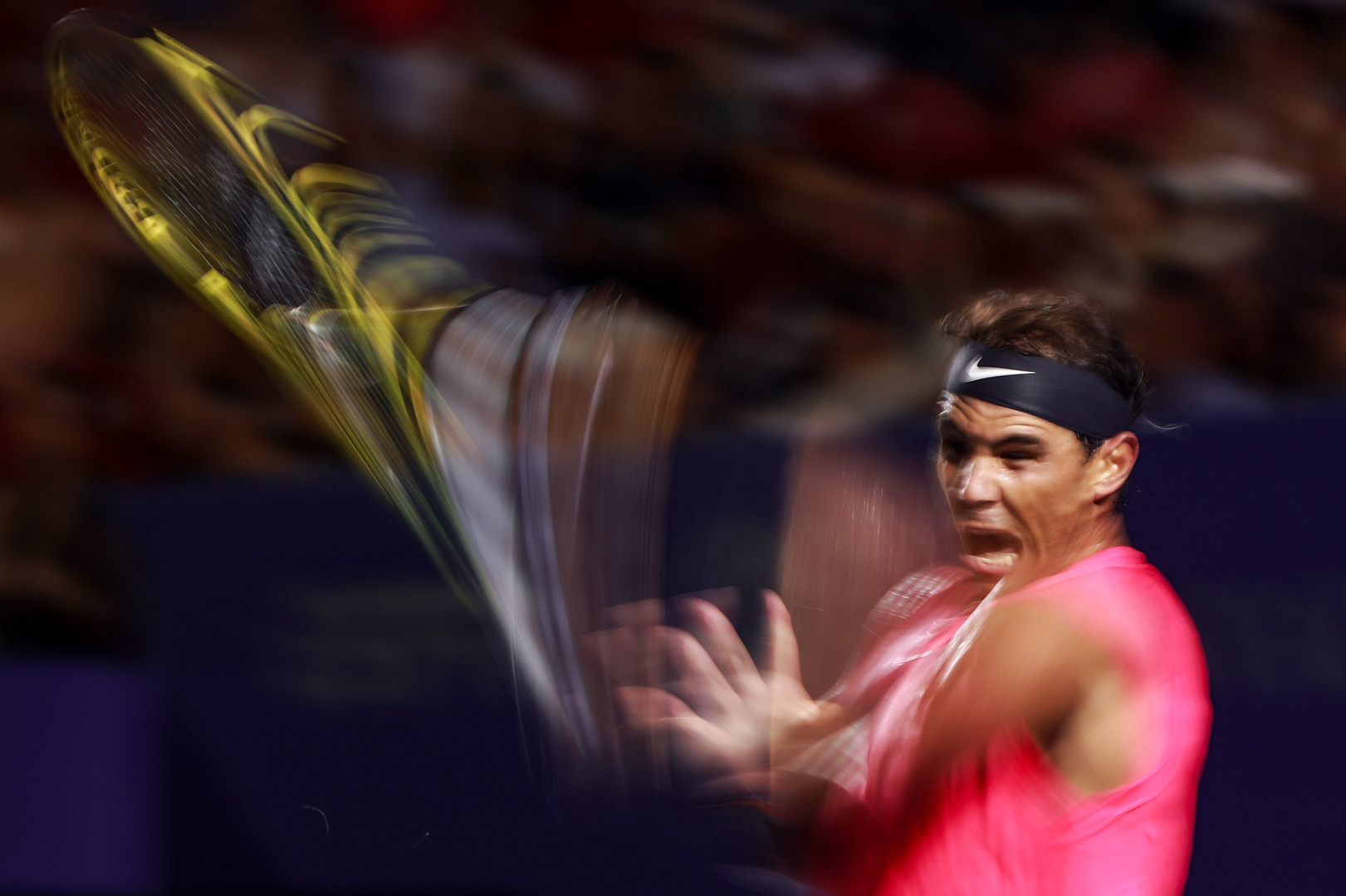 Blur and motion shot of Rafael Nadal hitting a tennis ball with his racquet.