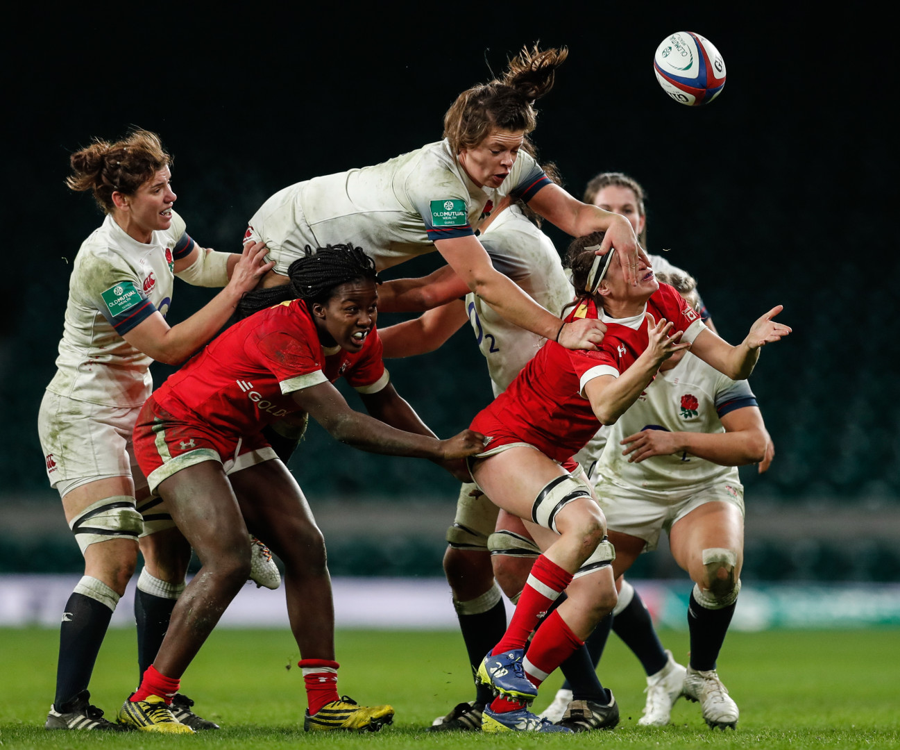 England women's rugby player jumping over opposition players whilst blocking their view with her hand.